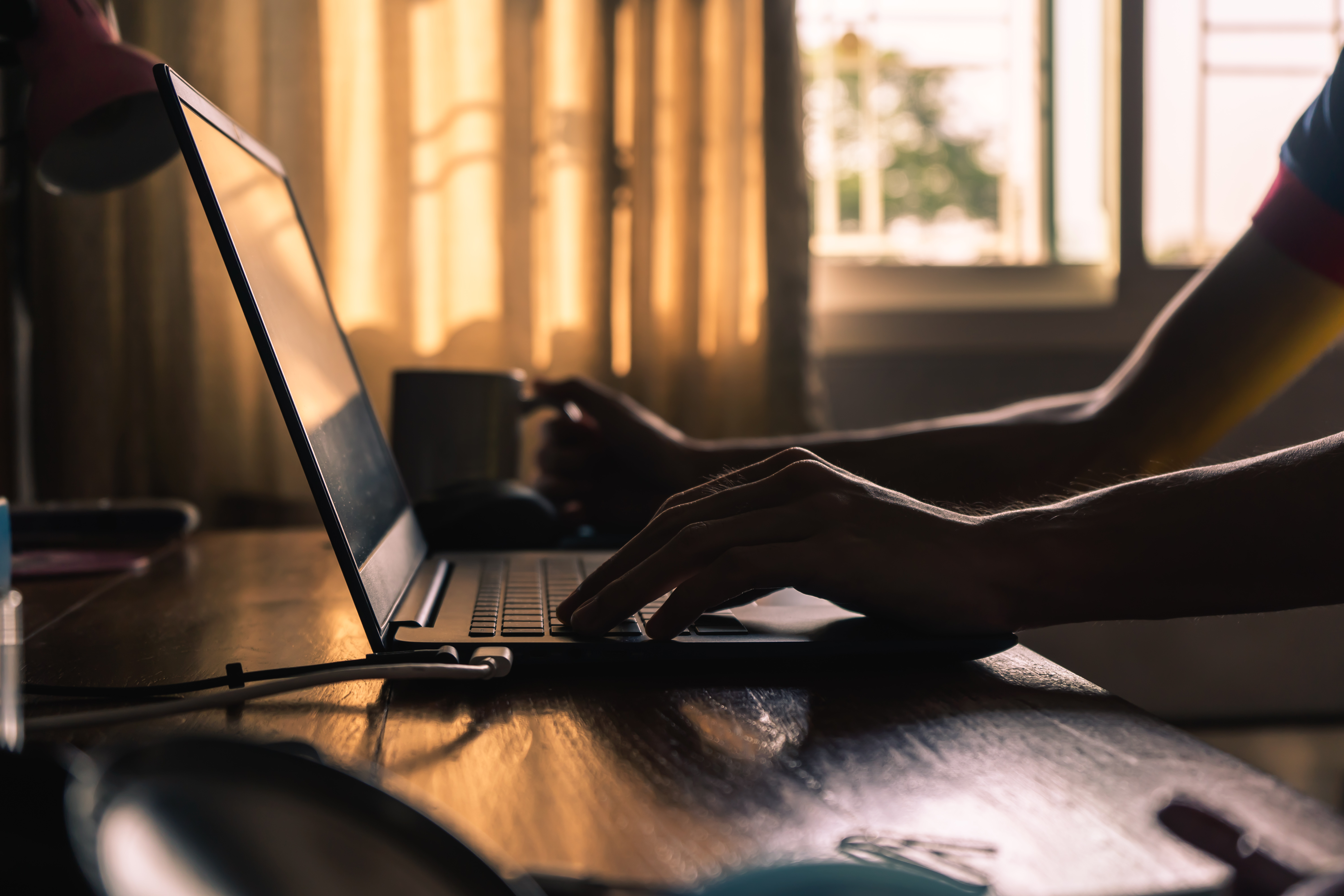 Silhouette of an unidentified individual sitting down at a laptop to work remotely. 