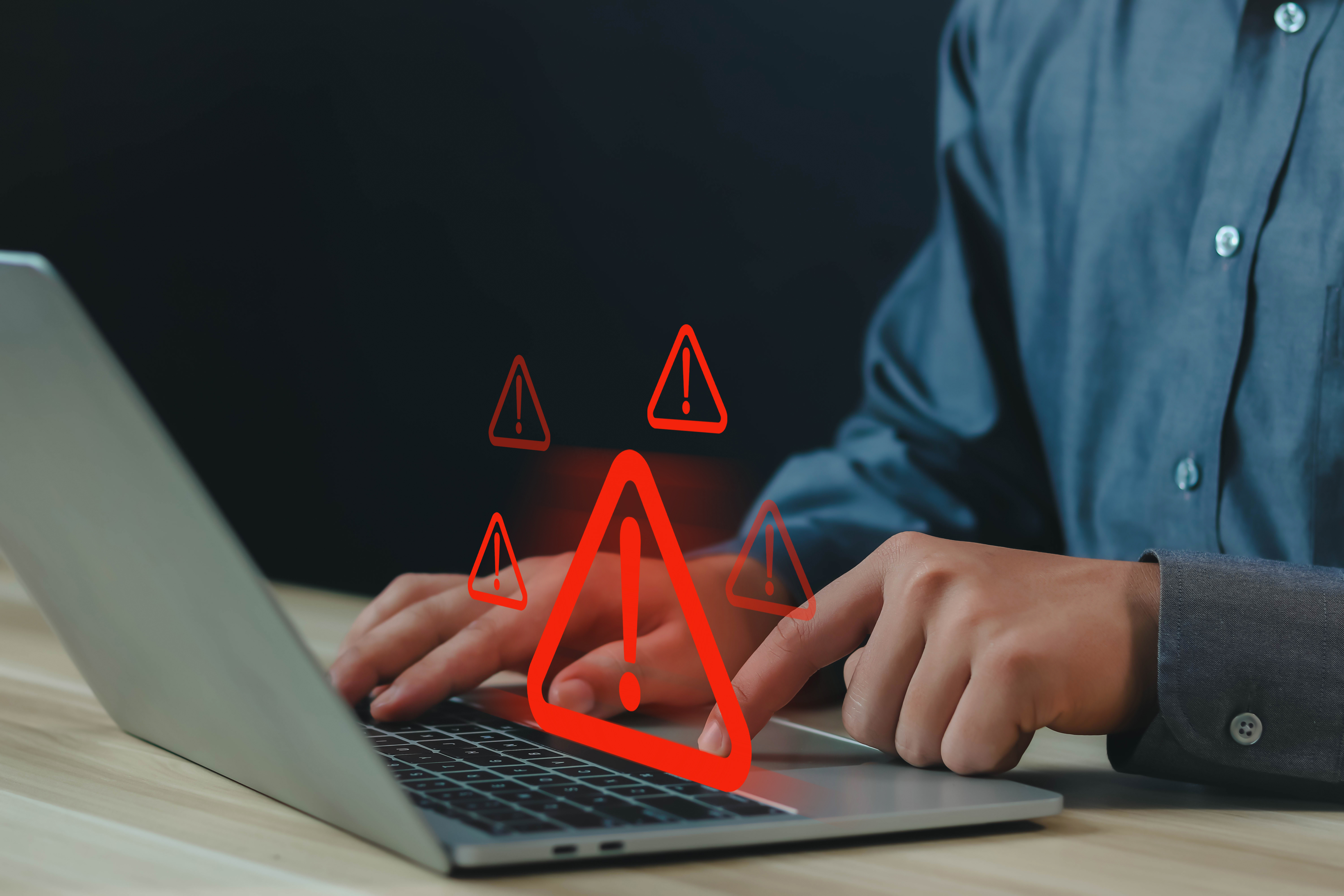 A person sitting at a keyboard with an overlay of red warning symbols indicating potential fraud