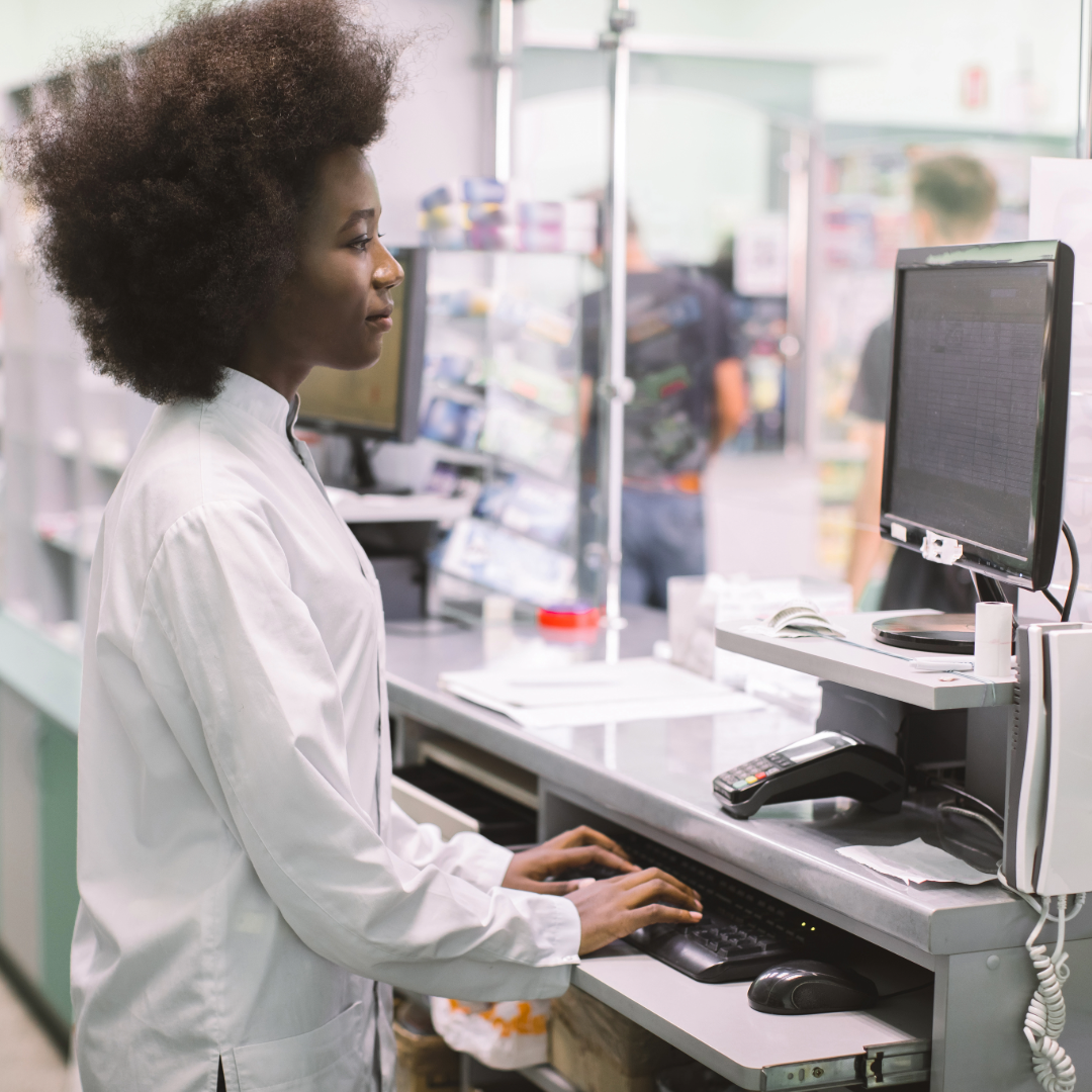 A pharmacist standing at a shared workstation.